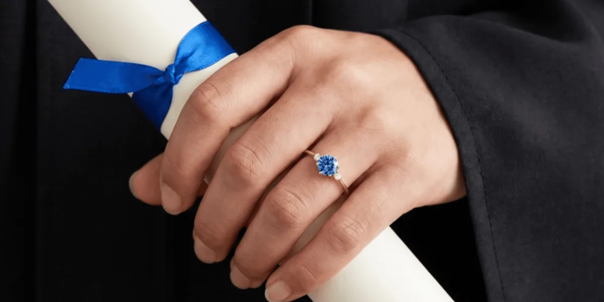 Formando de beca segurando o diploma e usando anel de formatura com pedra azul