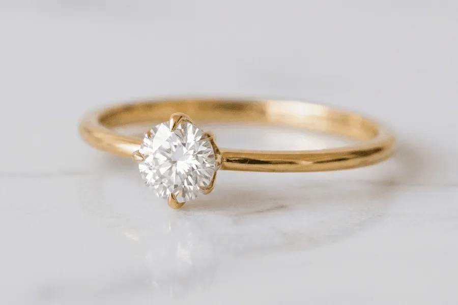 Anel de noivado solitário em ouro amarelo com diamante central sobre mármore